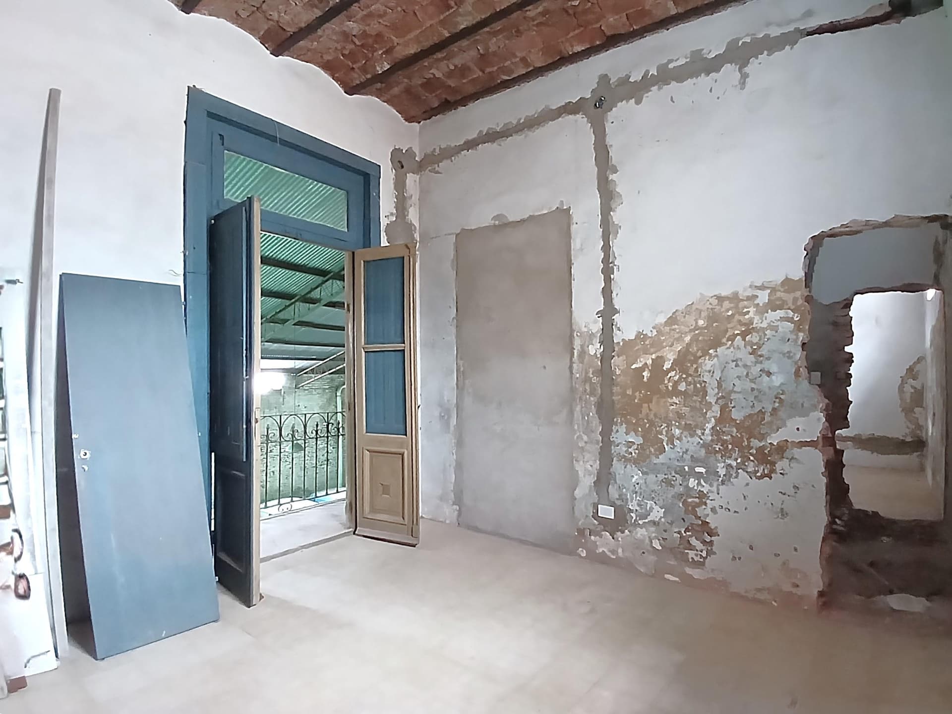 Dormitorio vacío en refacción con pared sin revocar y puerta a balcón.