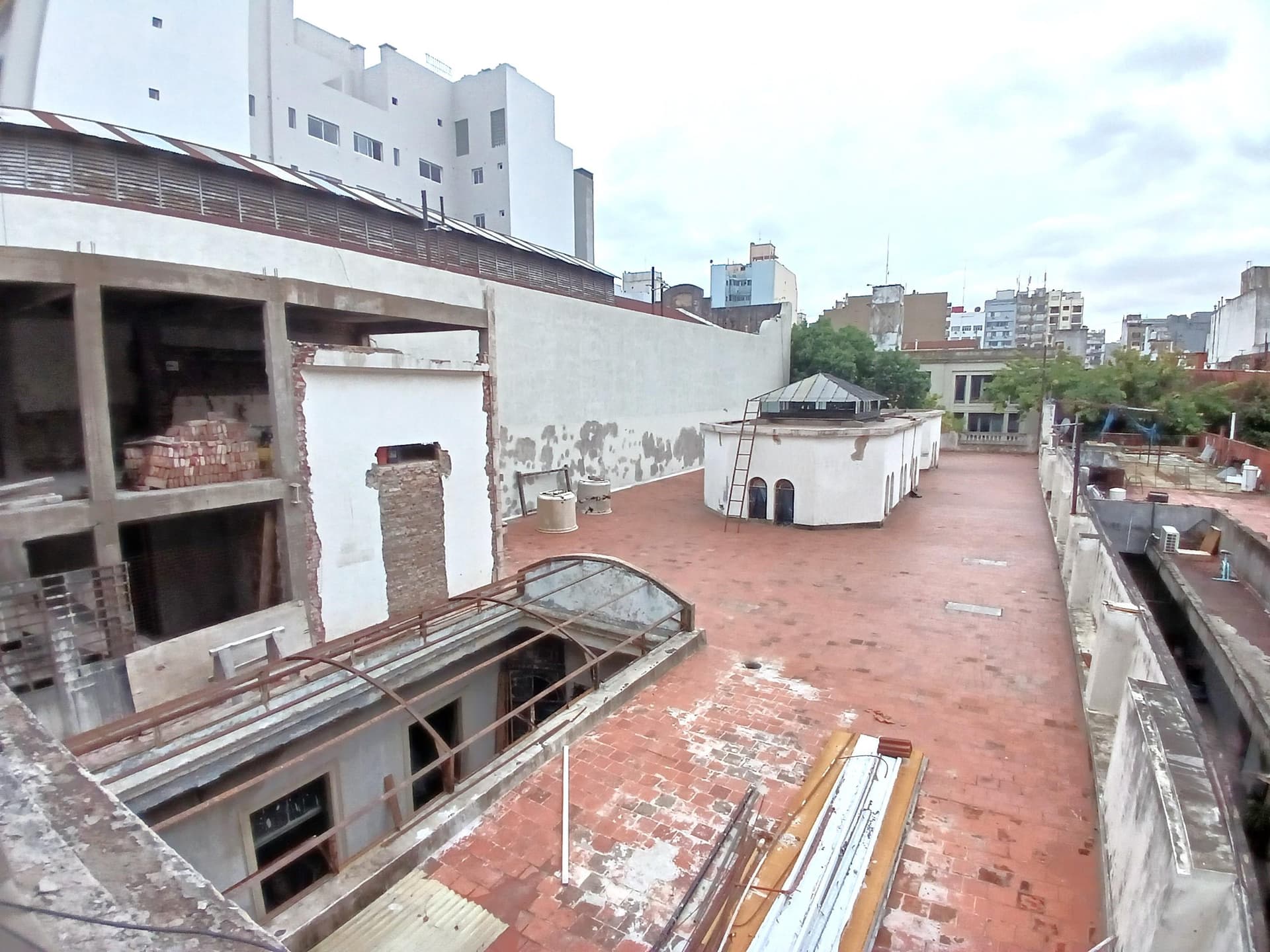 Terraza amplia con baldosas rojas y edificios circundantes bajo cielo nublado.