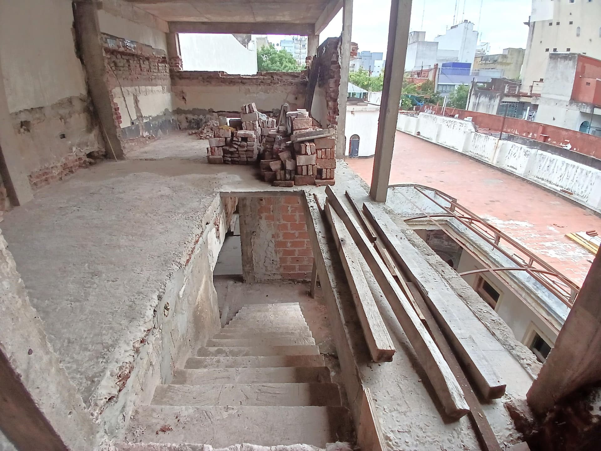 Escalera en obra con materiales de construcción y vista a la terraza.