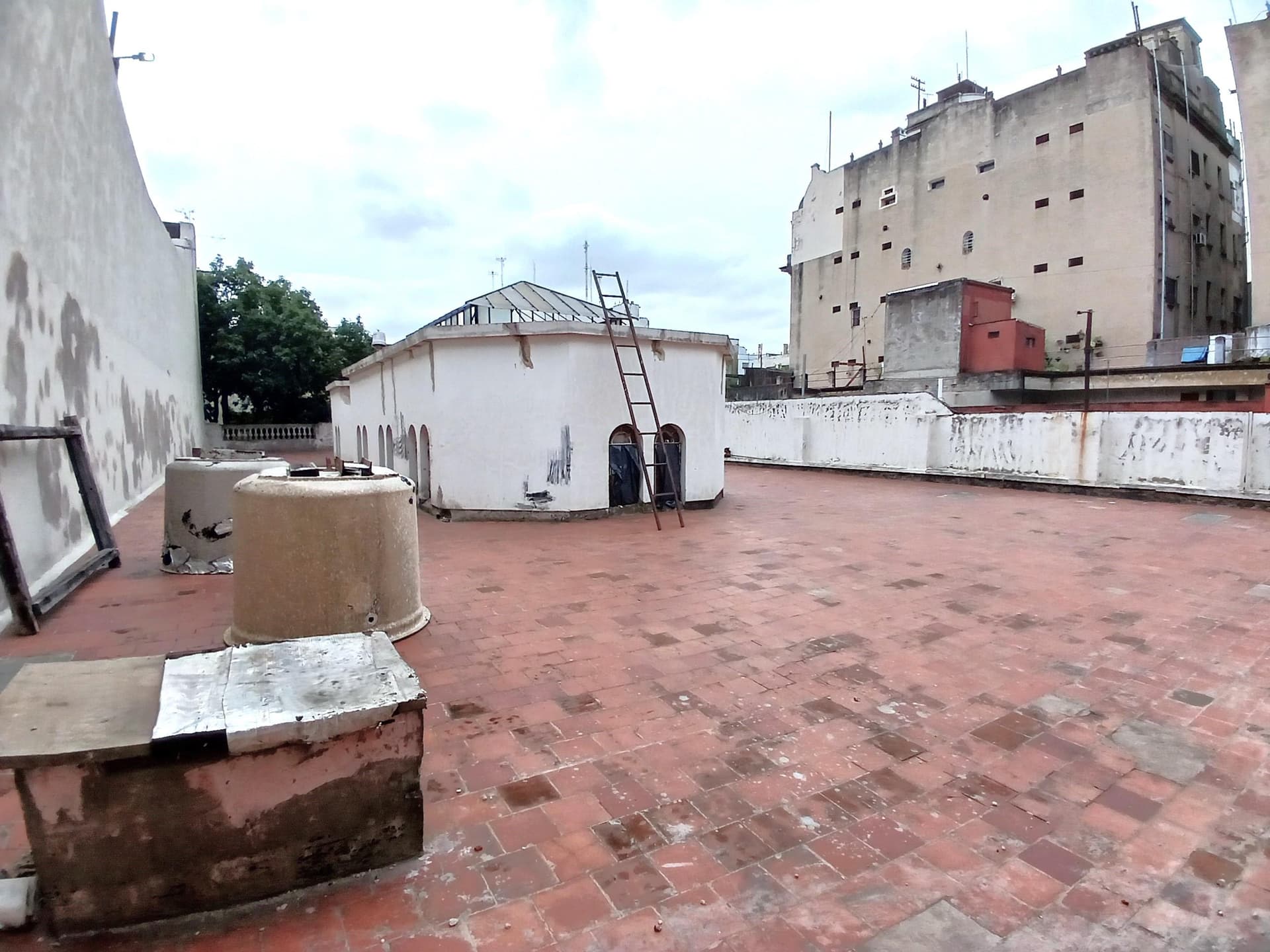 Terraza con baldosas rojas, cúpula redonda y edificios al fondo.