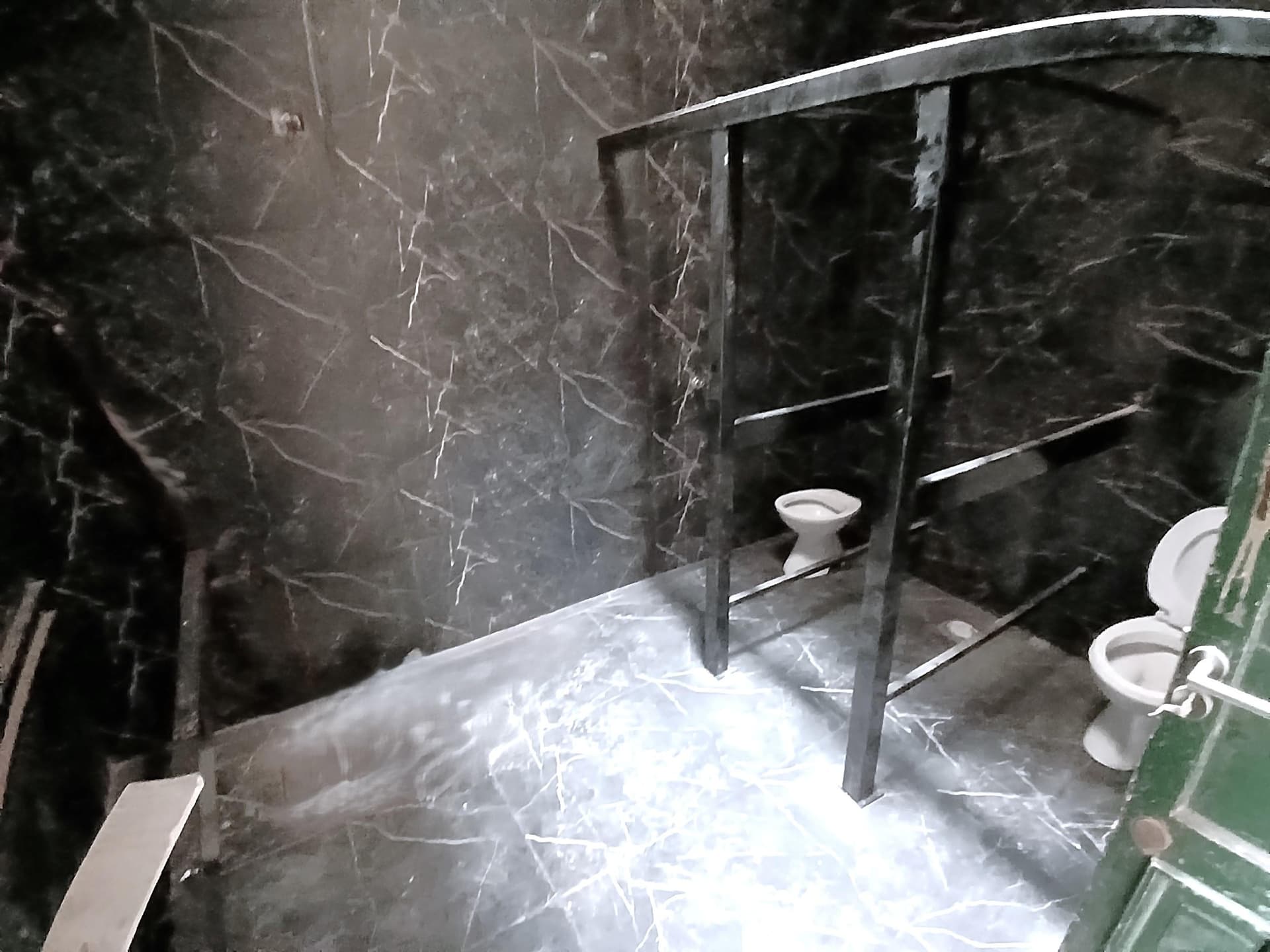 Baño público con dos inodoros y paredes de mármol negro.