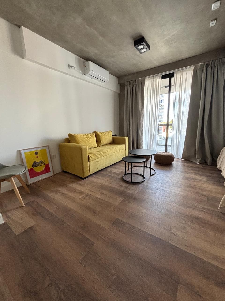 Living con sillón amarillo, mesa ratona y ventana grande con cortinas.