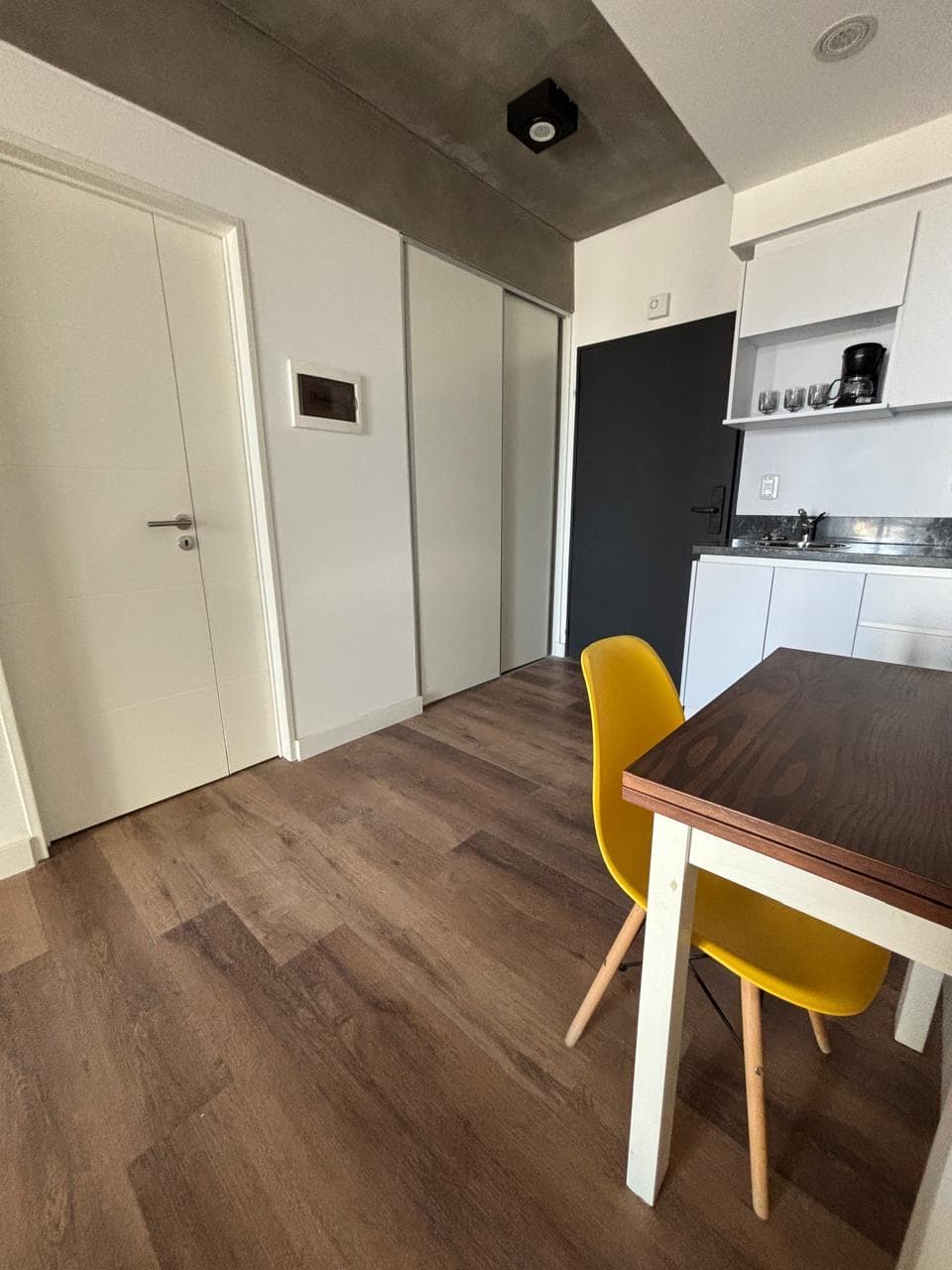 Área de comedor con mesa y silla amarilla, cerca de puertas.