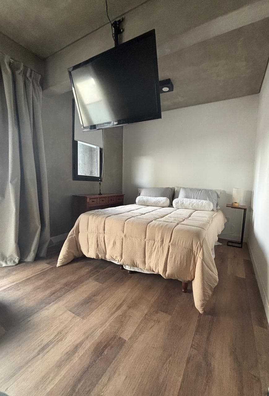 Dormitorio con cama doble, televisor colgante y ventanas con cortinas.