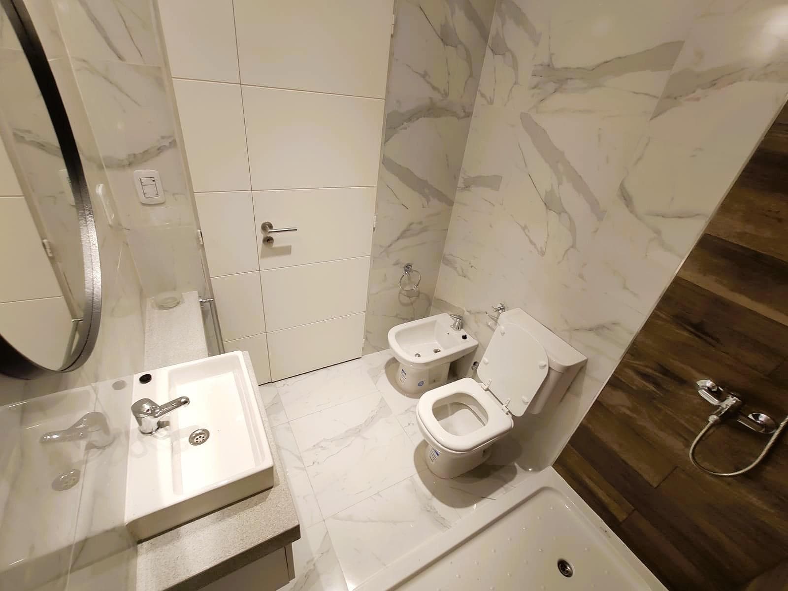 Baño con inodoro, bidet, vanitory y espejo redondo.