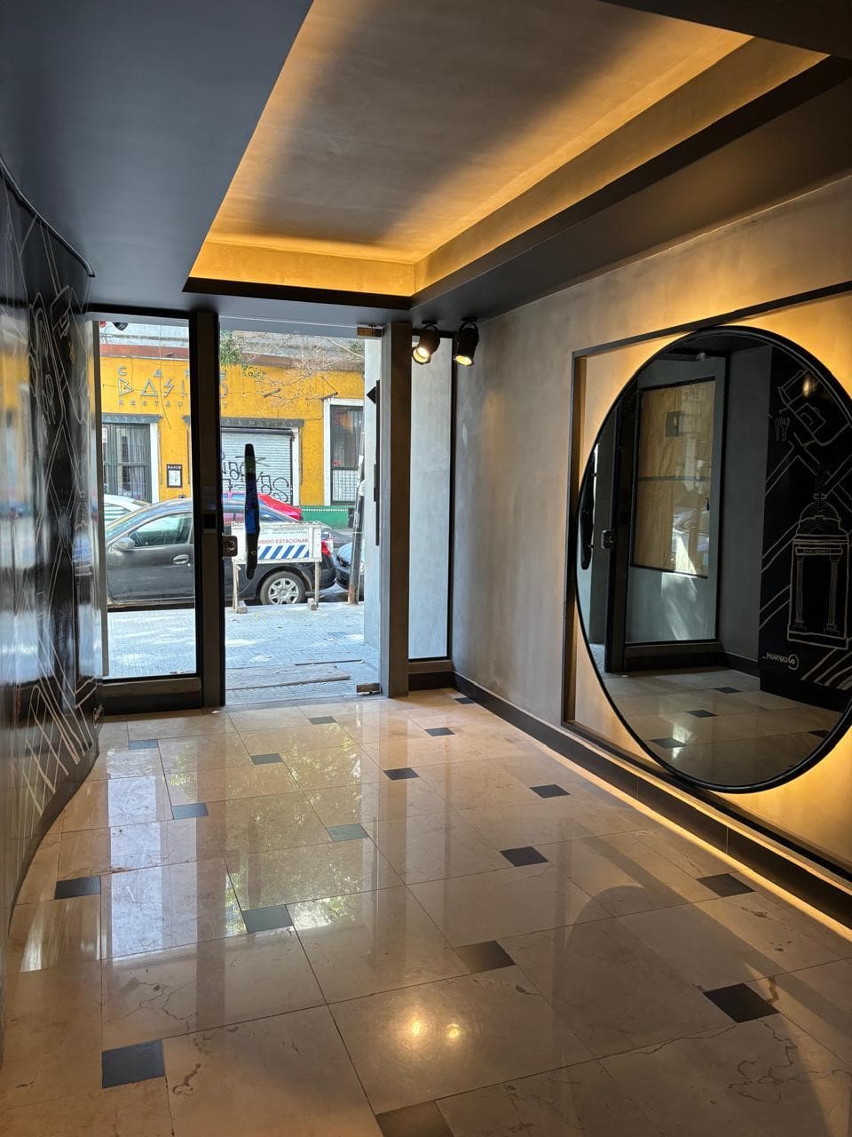 Hall de entrada del edificio con espejo redondo y piso de baldosas.