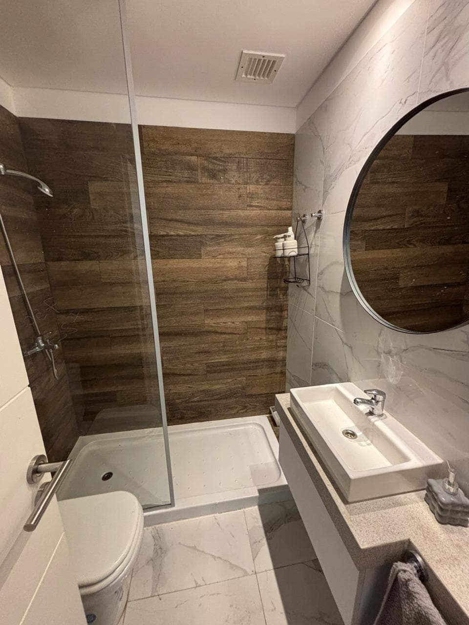 Baño con vanitory, espejo y ducha con azulejos de madera.