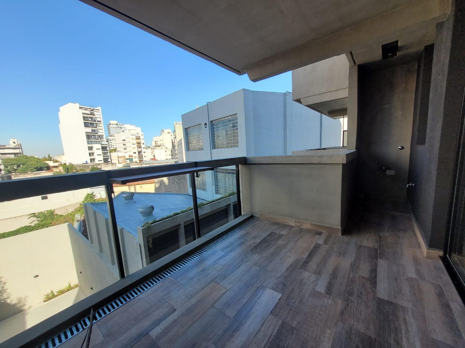 Balcón amplio con piso de madera y vista urbana.