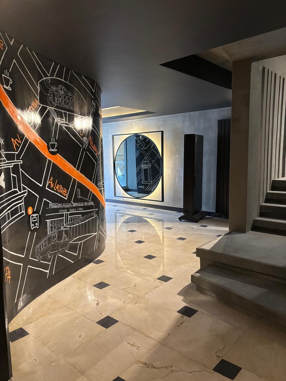 Hall de entrada con mural decorativo, espejo circular y escaleras.