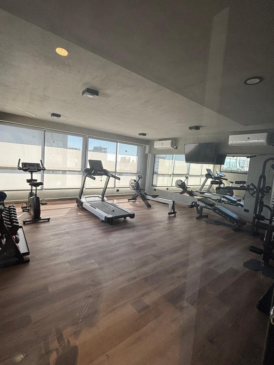 Gimnasio con varias máquinas de ejercicio y ventanales.
