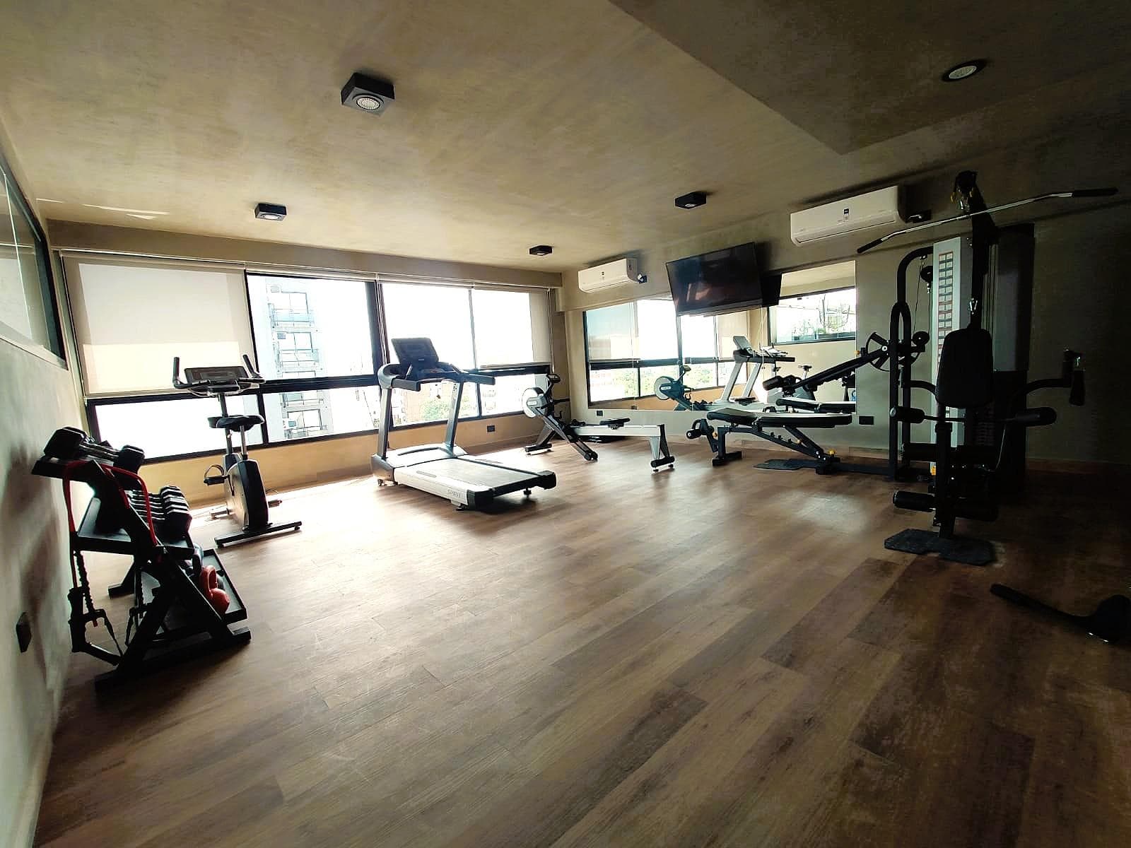 Gimnasio completo con cintas, bicicletas, pesas y amplia vista.