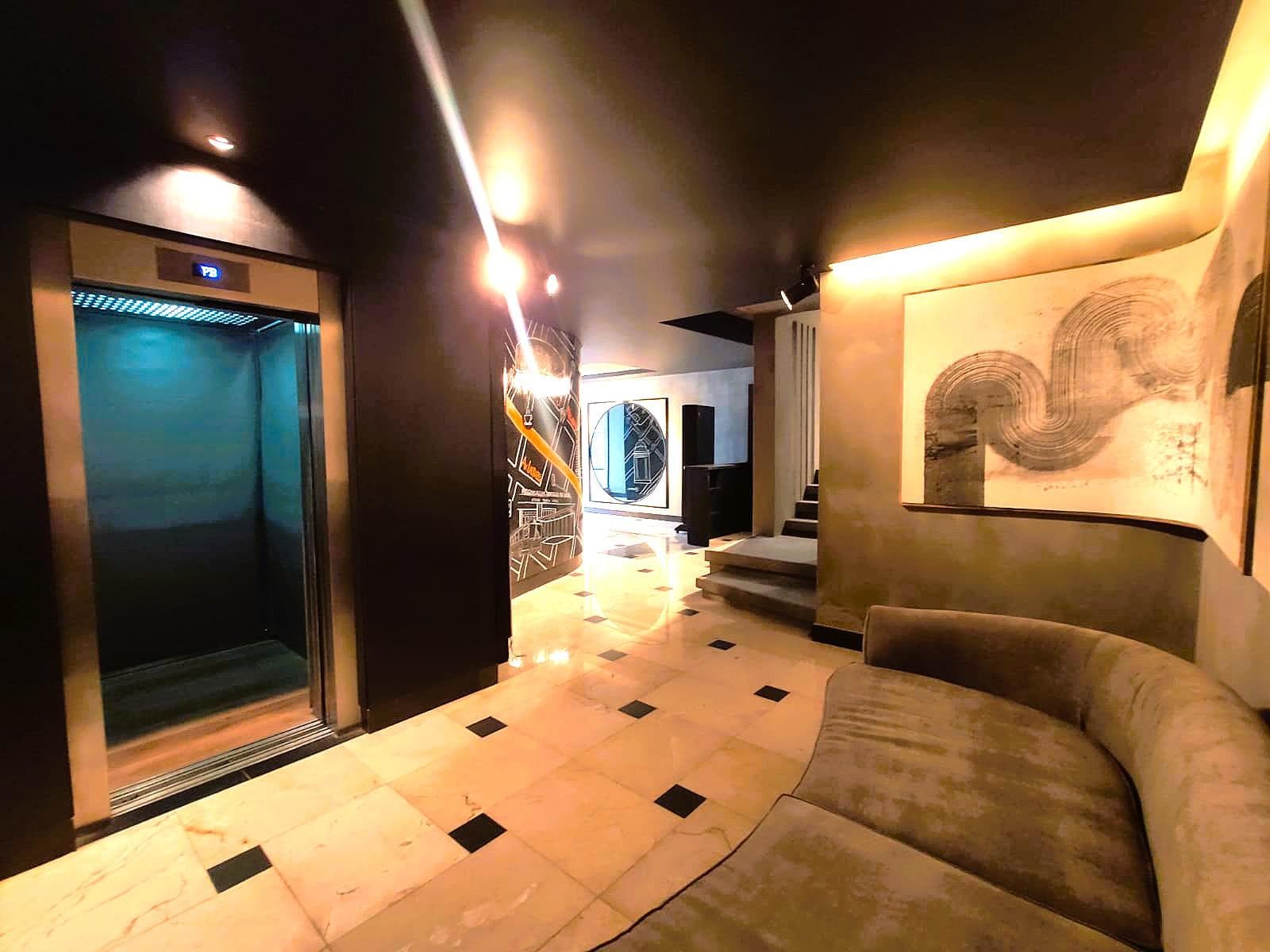 Hall de entrada con ascensor, sillón curvo y obras de arte.