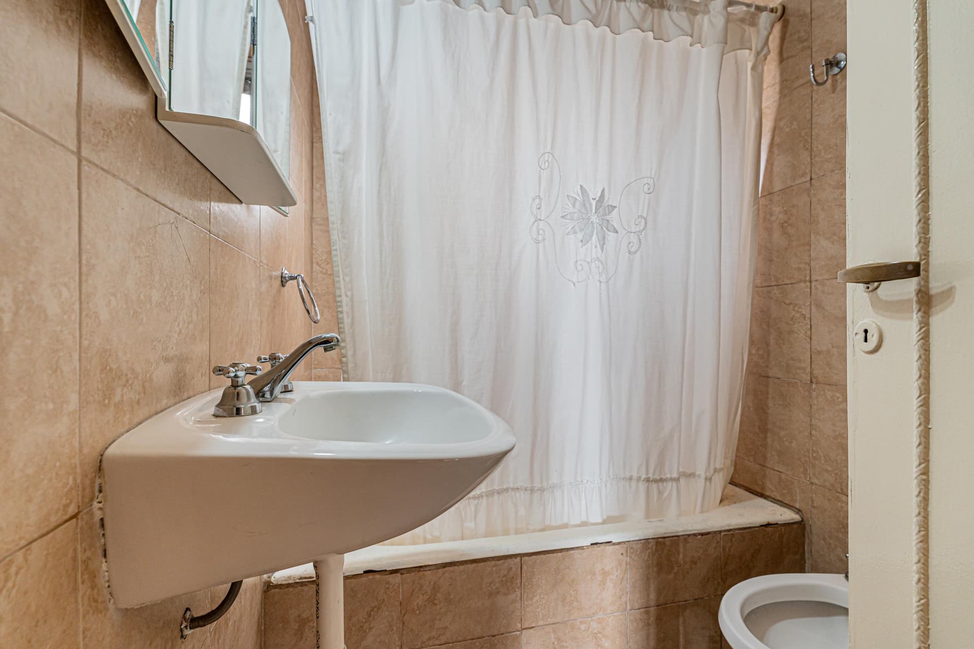 Baño con lavatorio, bañera con cortina y azulejos en tonos tierra.