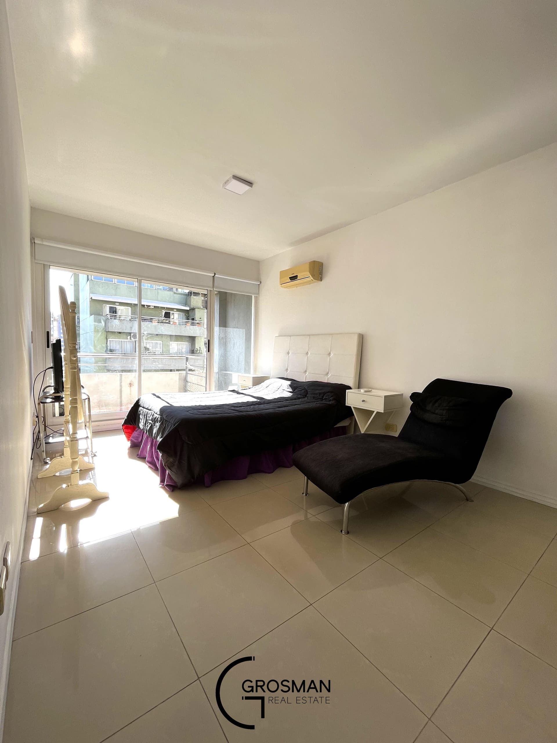 Dormitorio con cama doble, chaise longue y acceso al balcón.