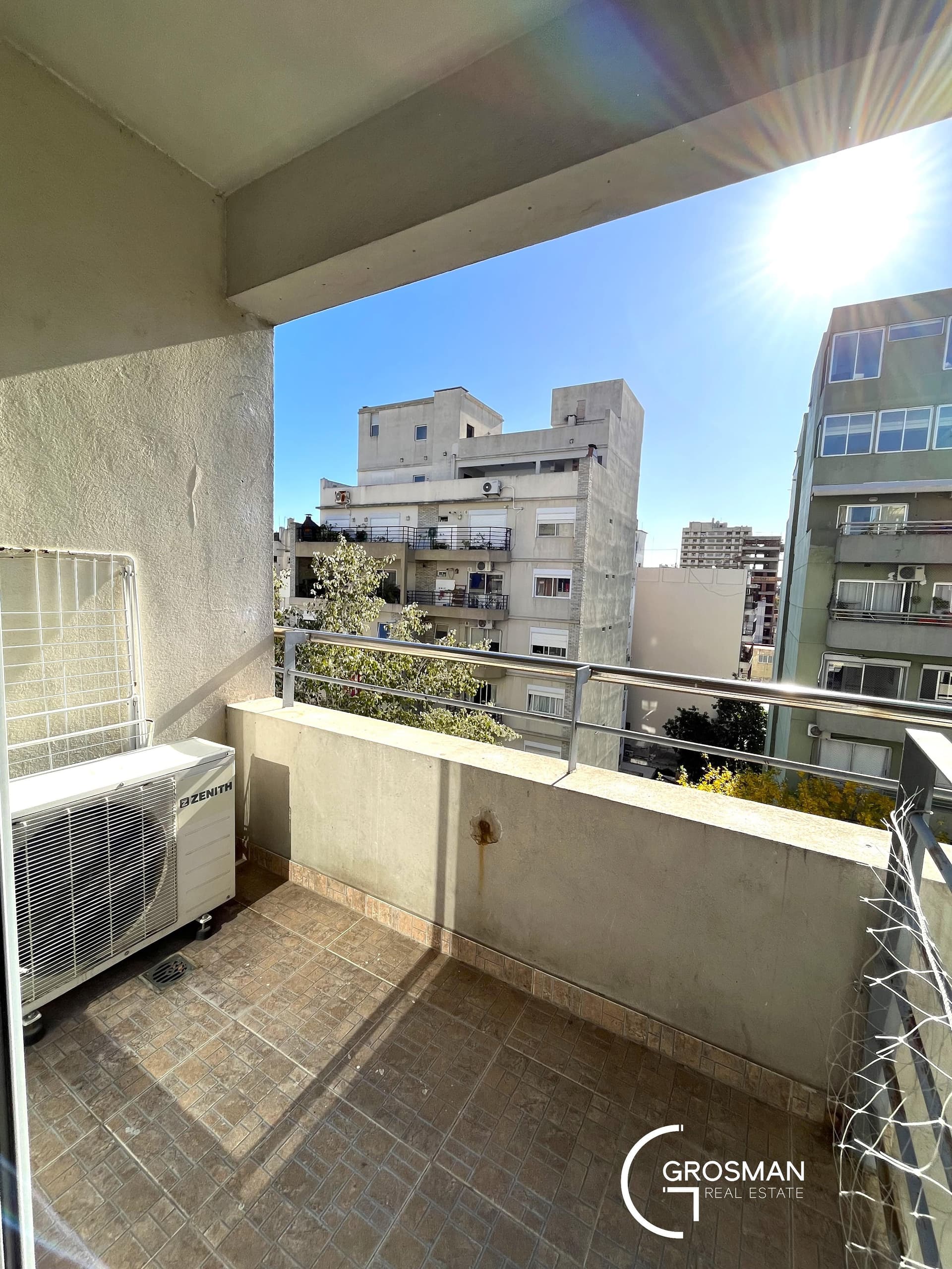 Balcón con unidad de aire acondicionado y vista a edificios cercanos.