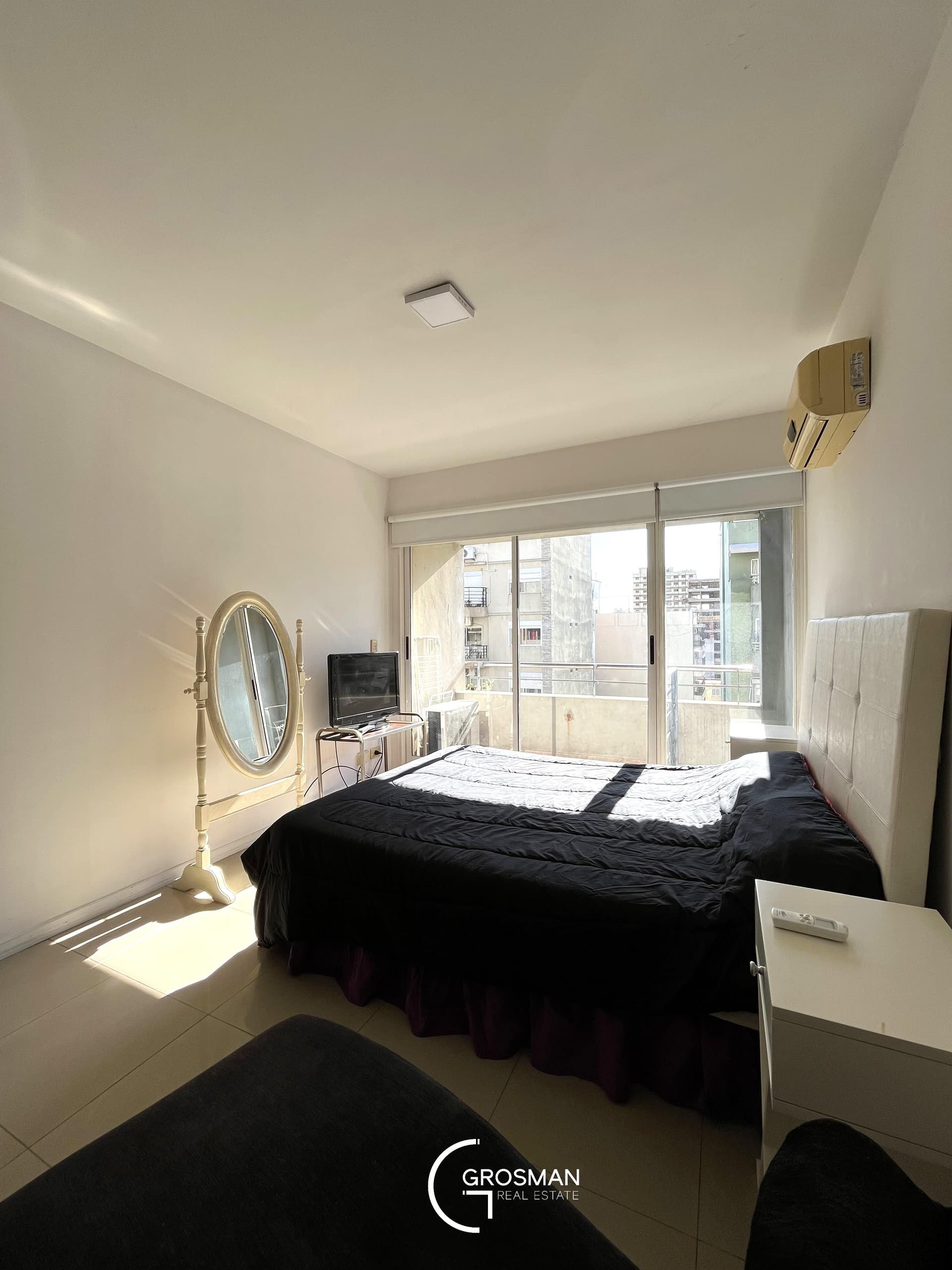 Dormitorio con cama doble, espejo y ventana con salida al balcón.