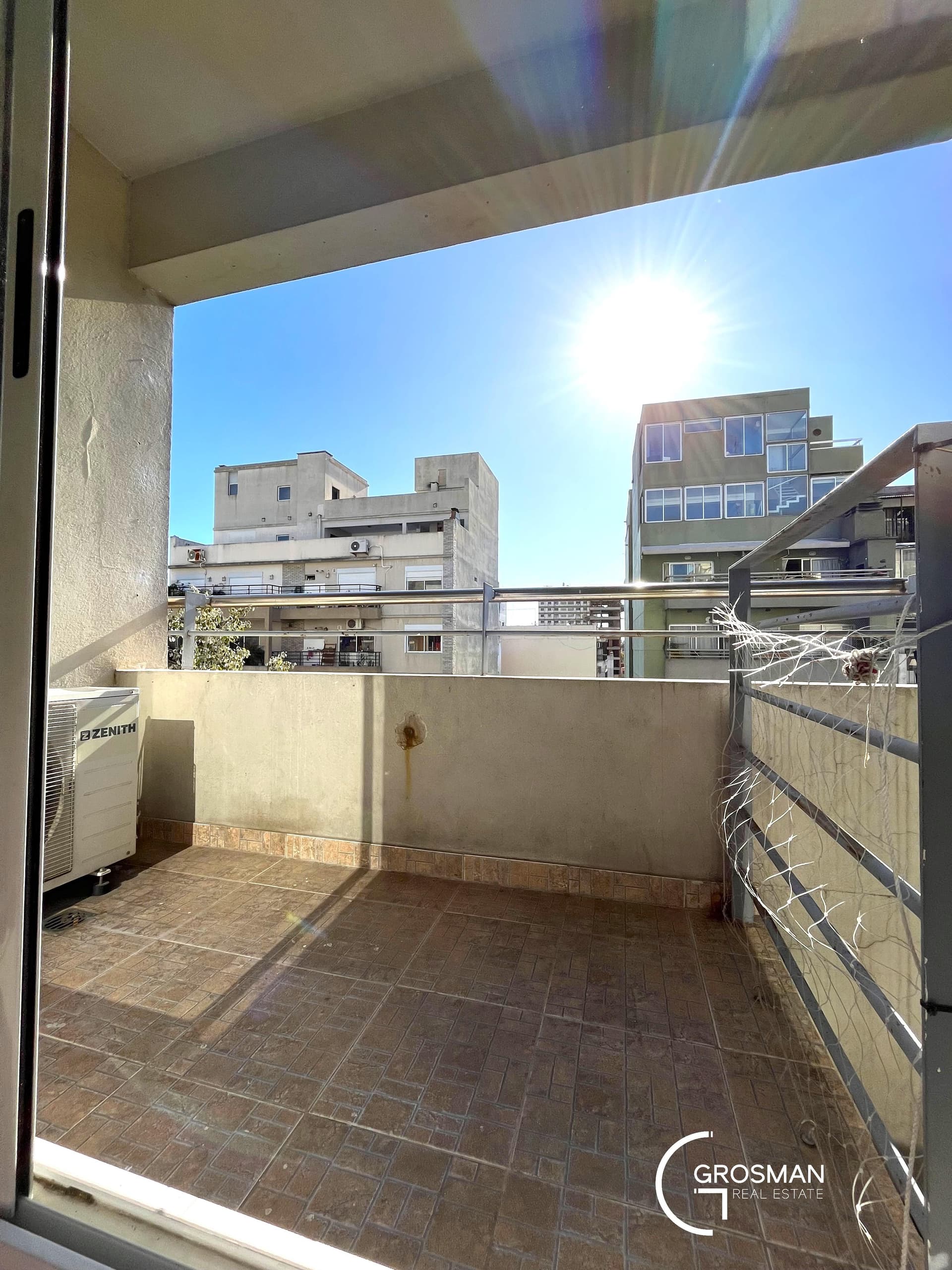 Balcón exterior con vista a otros edificios y unidad de aire.