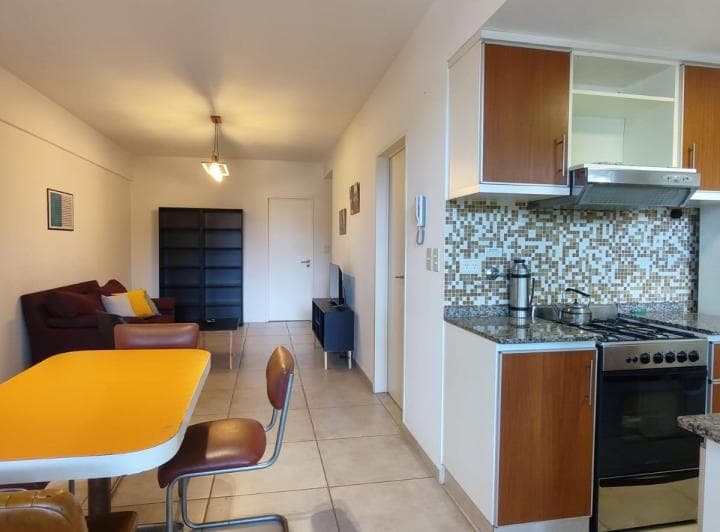 Cocina integrada con horno, anafe, alacenas de madera y mesa comedor.