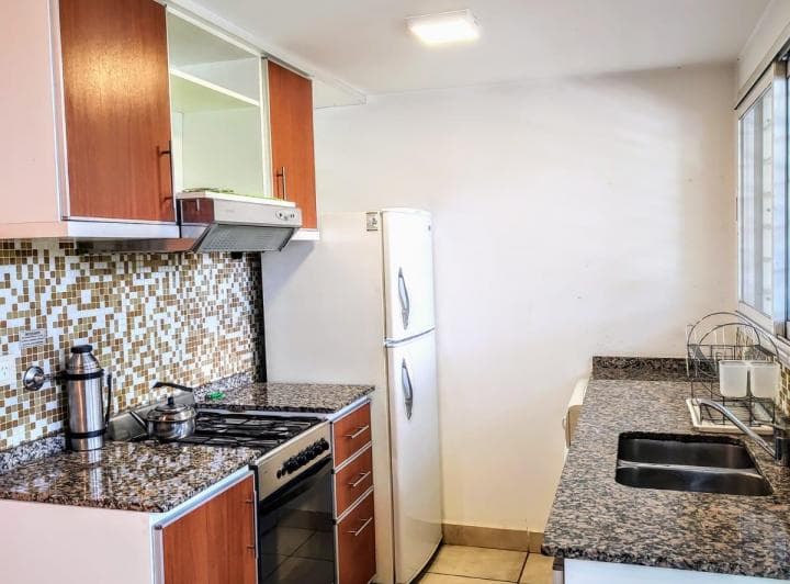 Cocina con heladera, bacha, mesada de granito, anafe y alacenas de madera.