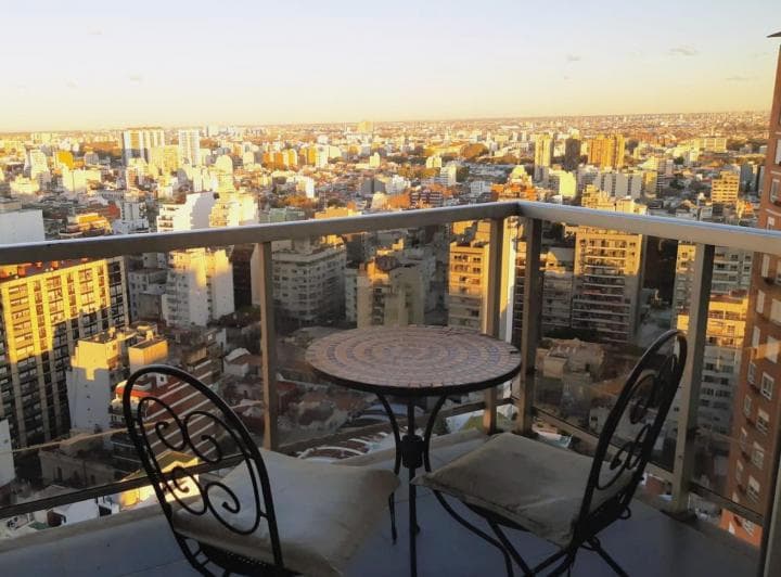 Balcón con mesa y sillas de hierro forjado, vista panorámica a la ciudad.