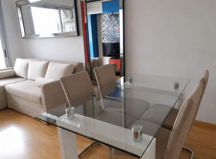 Comedor con mesa de vidrio y sillas, parte de un sofá en el fondo.