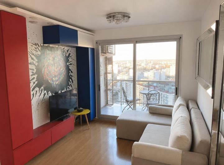 Living con sofá, mueble de TV rojo, cuadros y acceso a balcón con vista.