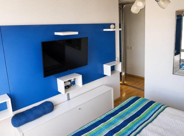 Dormitorio con cama, pared azul, televisión y placard con espejo.
