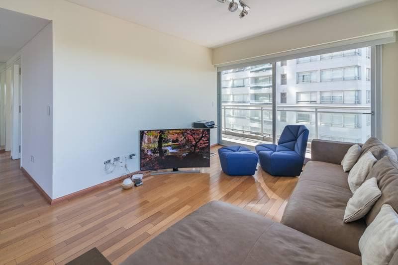 Living con televisión y sillón en L, con una puerta al pasillo.