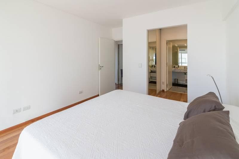 Dormitorio con cama doble, piso de madera y puerta que lleva al baño en suite.