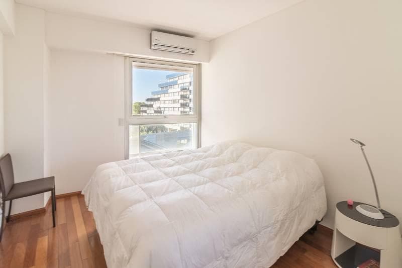 Dormitorio con cama, acolchado blanco, ventana y aire acondicionado.