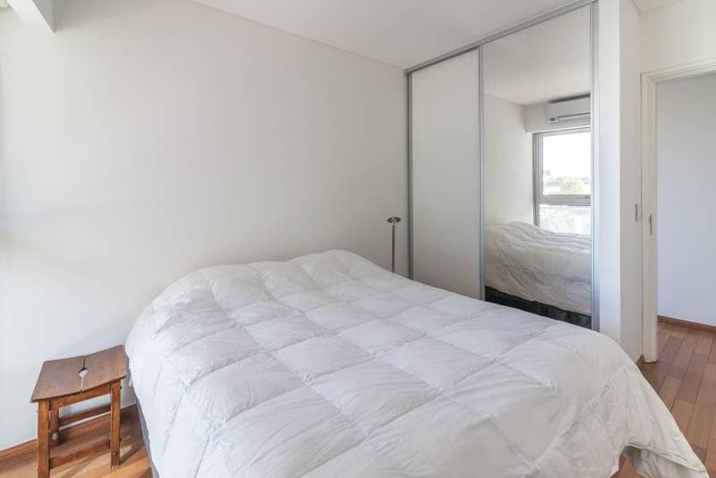 Dormitorio con cama y acolchado blanco, placard espejado y piso de madera.
