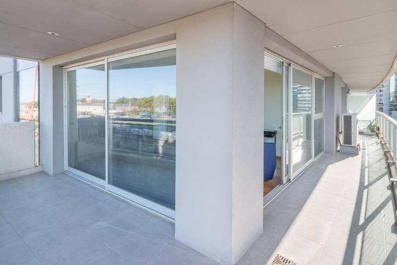 Balcón espacioso con piso de cerámica, ventanales corredizos y vista exterior.