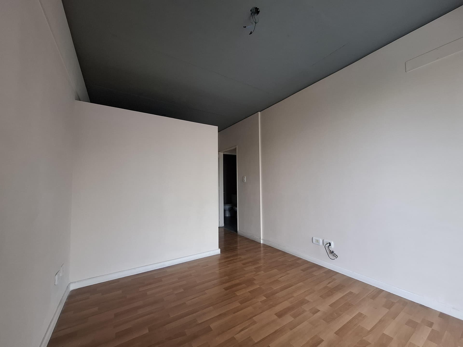 Dormitorio con piso de madera, vista a un pasillo oscuro.