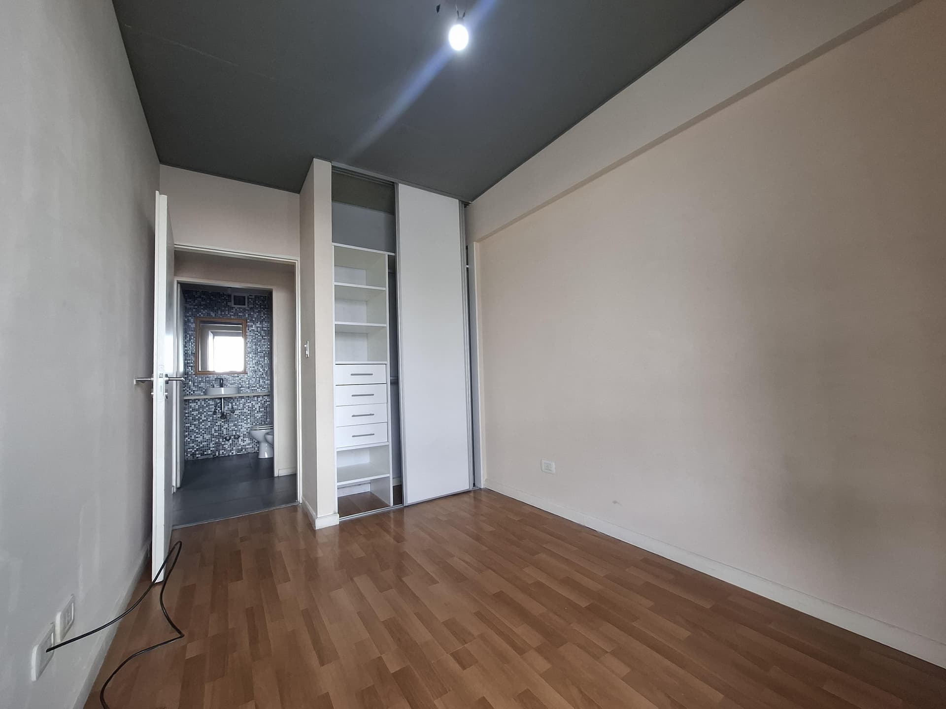 Dormitorio con placard y piso de madera, puerta a baño.