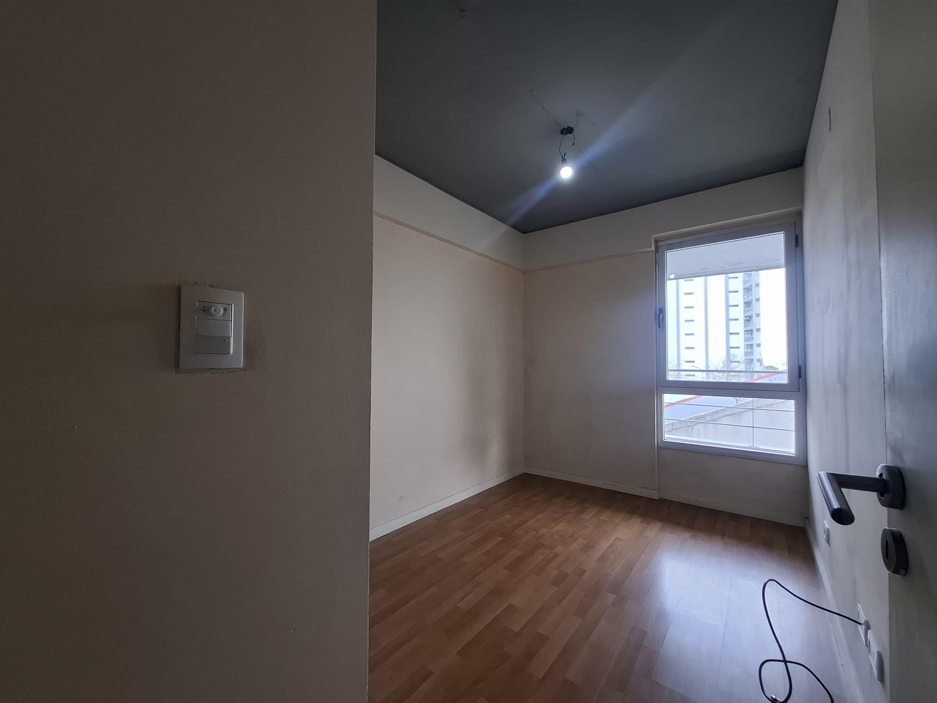 Dormitorio con ventana, piso de madera, paredes de color claro.