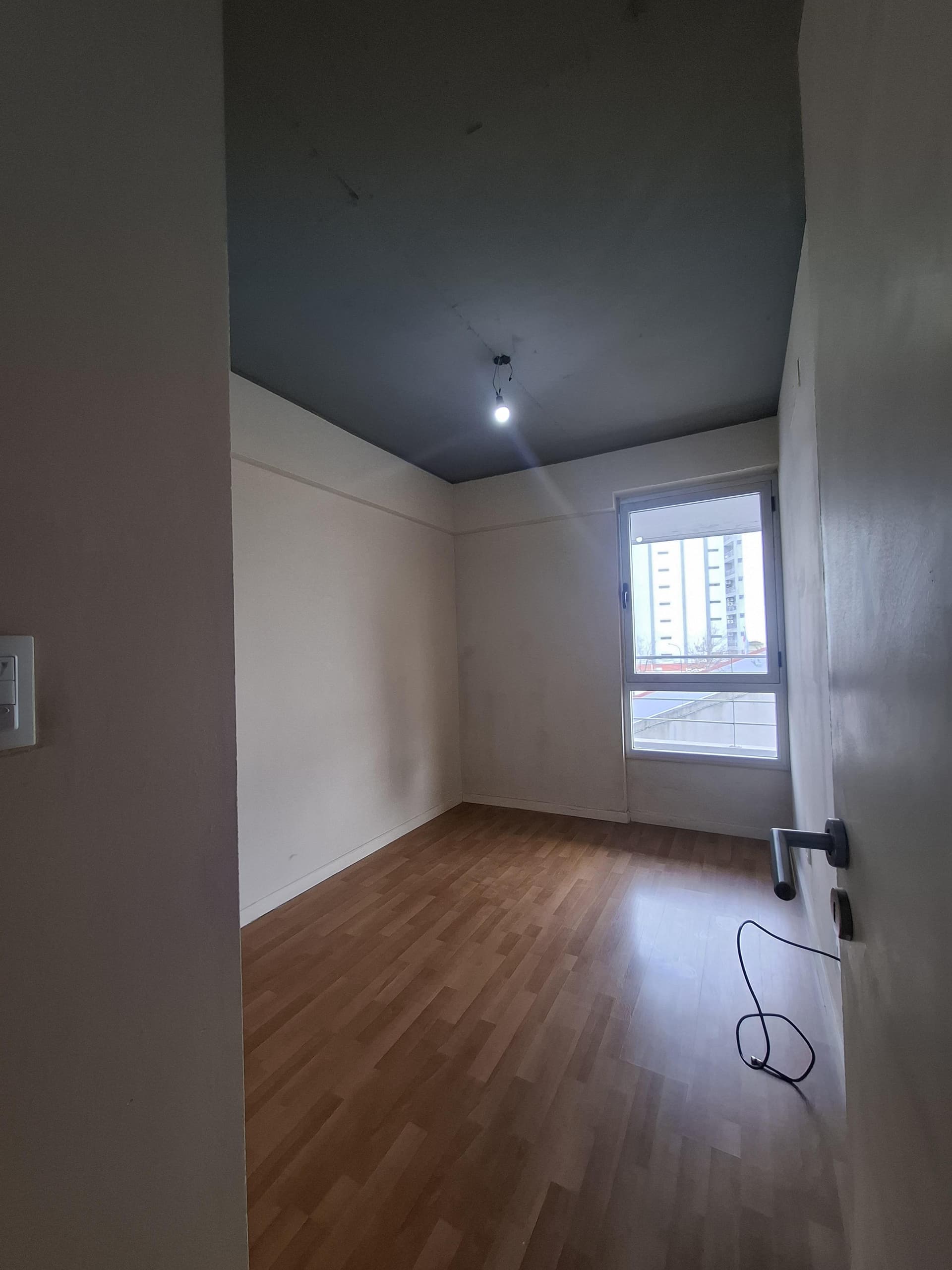 Dormitorio con ventana, piso de madera, puerta abierta a la derecha.