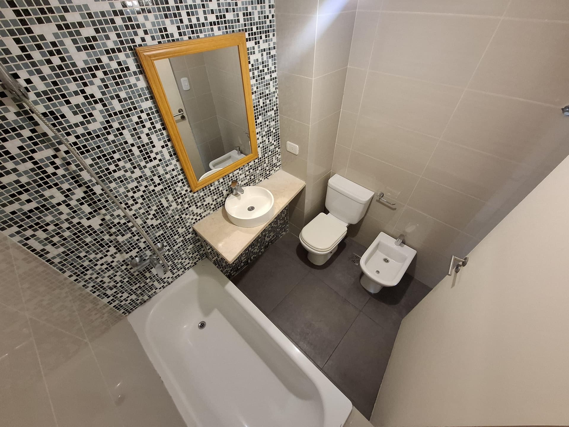 Baño completo con bañera, bidet, inodoro, vanitory y mosaicos.