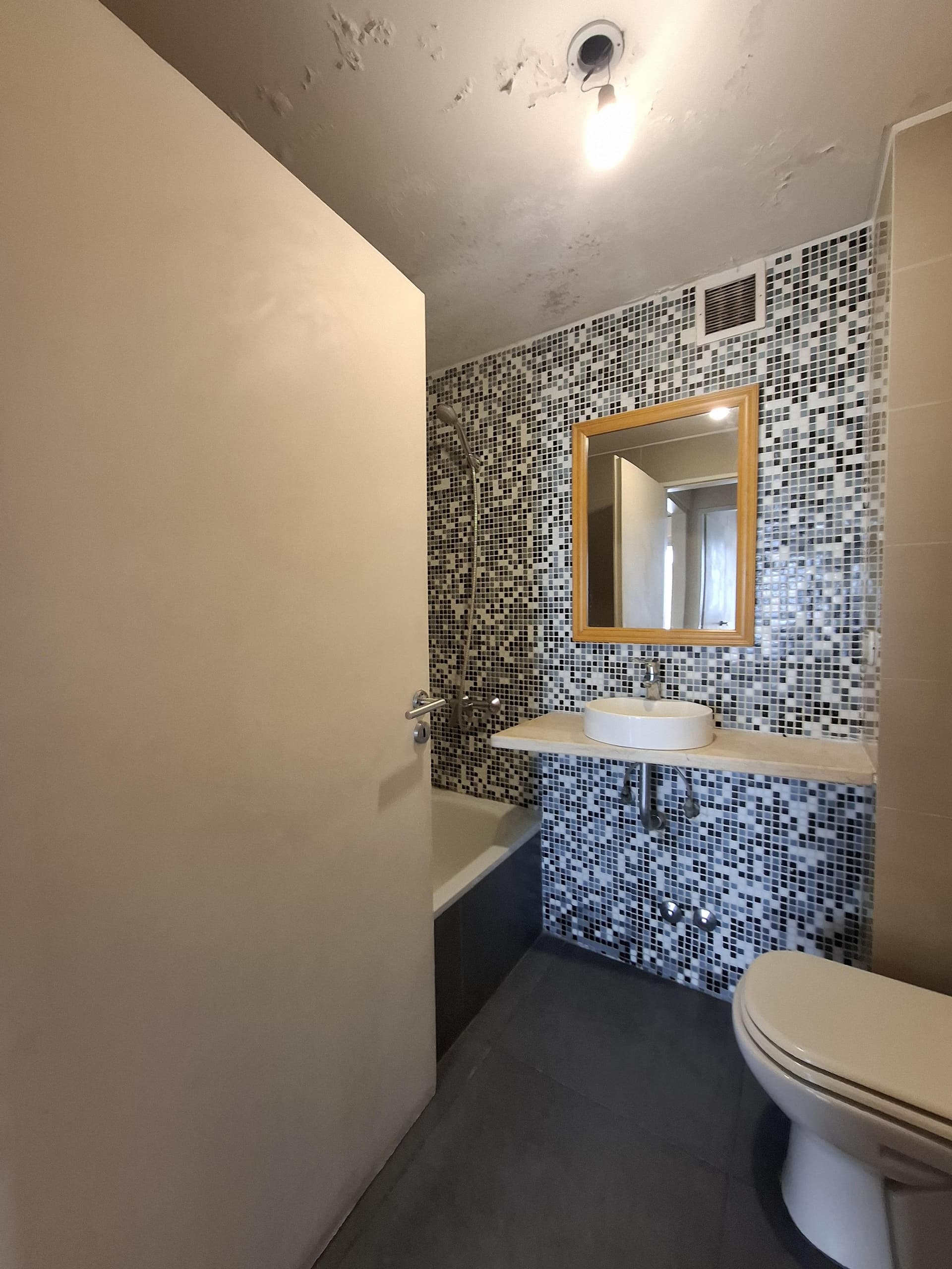 Baño con bañera y ducha, azulejos de mosaico blanco y negro.
