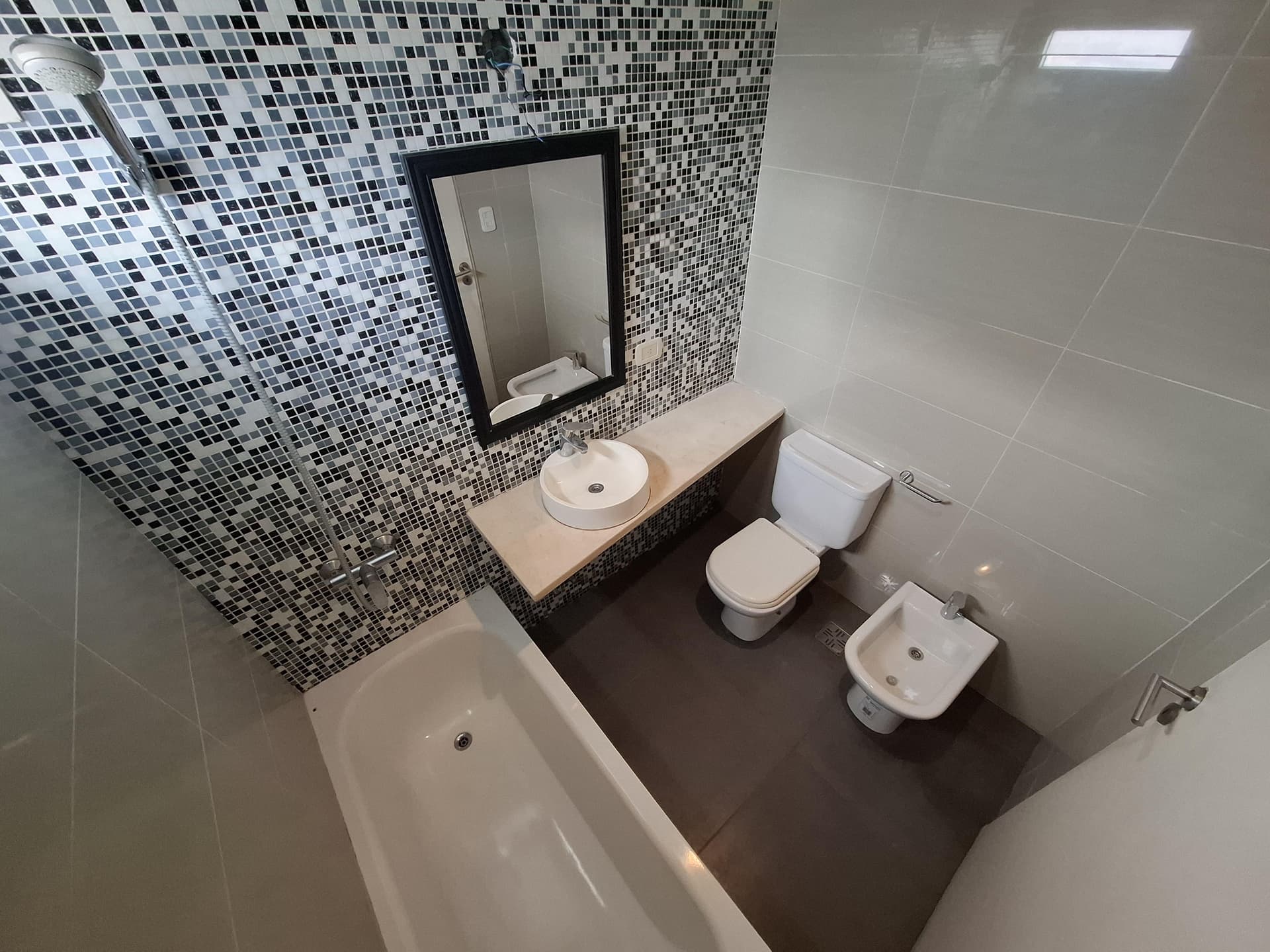Baño con bañera, bidet, inodoro y espejo, azulejos de mosaico.