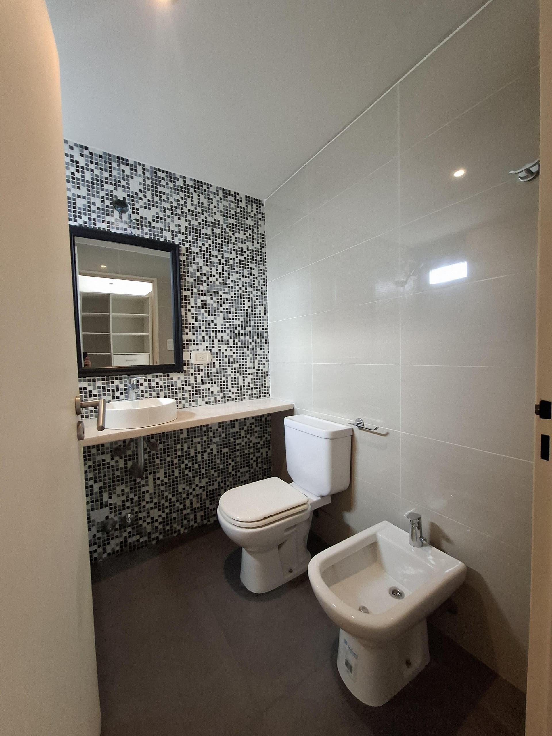 Baño con bidet, inodoro, vanitory, espejo y mosaicos.