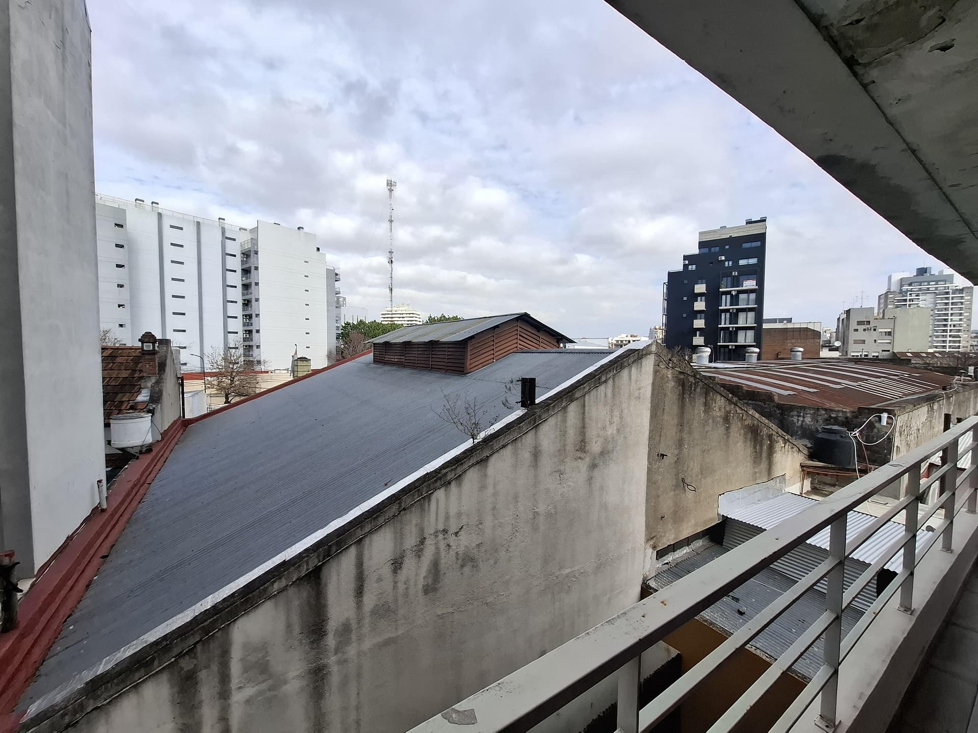 Vista urbana desde el balcón con techos de edificios y cielo nublado.
