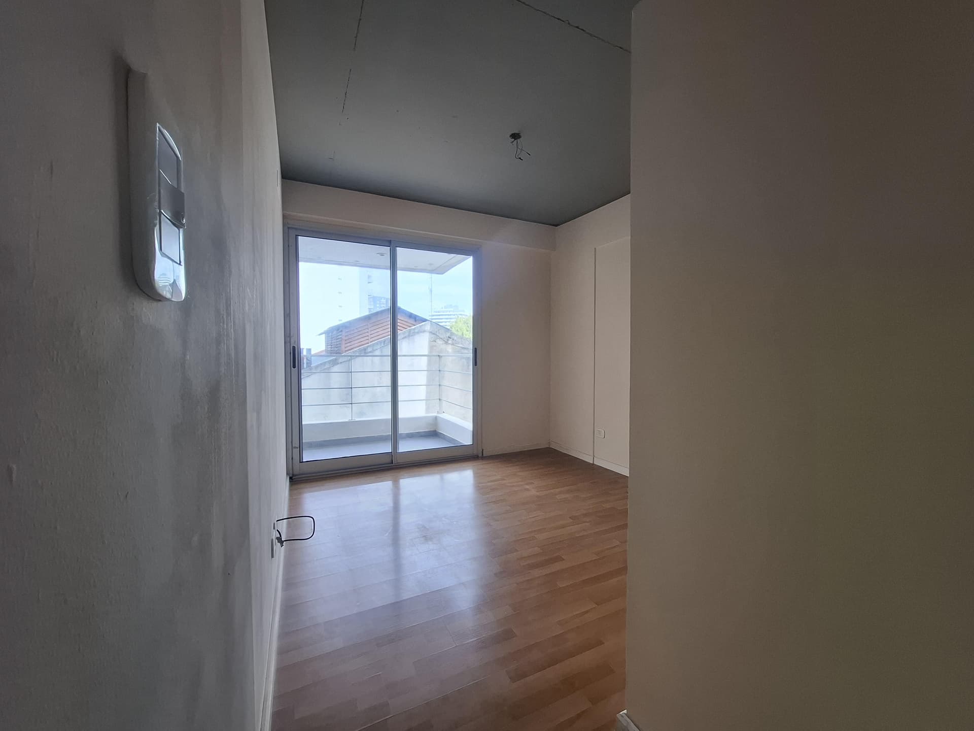 Dormitorio vacío con piso de madera y salida a un balcón.