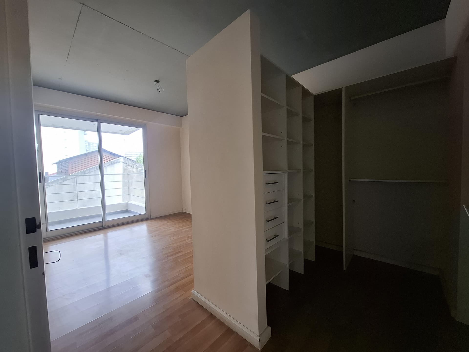 Dormitorio con vestidor abierto y balcón, piso de madera.