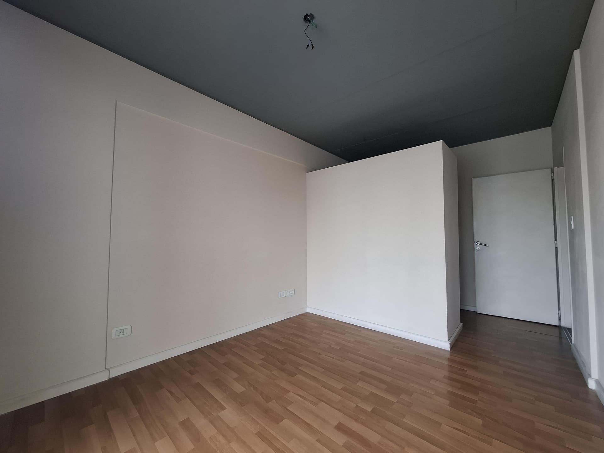 Dormitorio vacío con piso de madera y paredes claras.