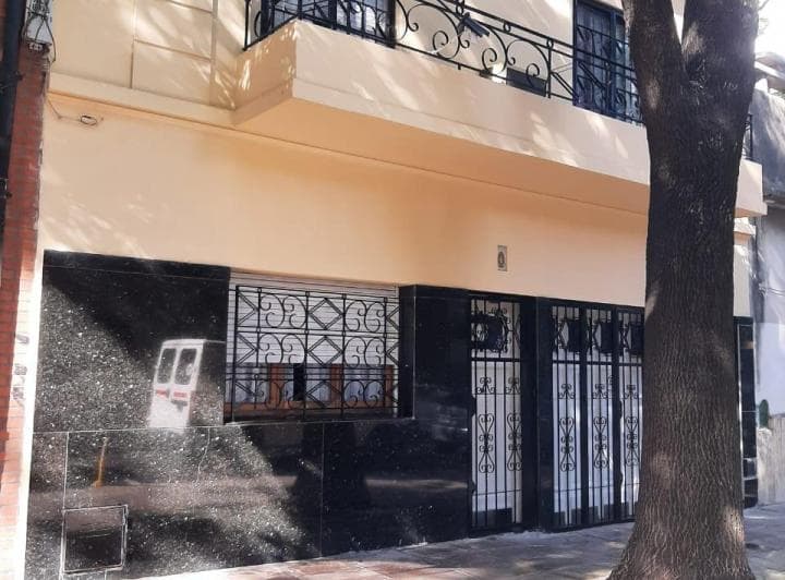 Fachada de PH con rejas negras y balcón en primer piso, árbol al frente.