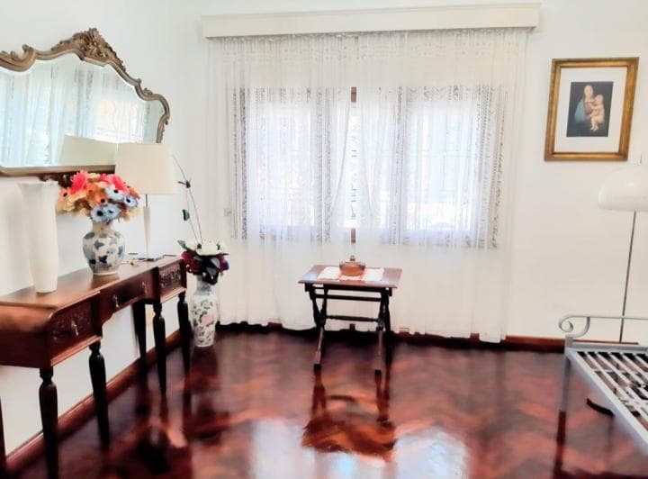 Living con piso de madera, ventana con cortinas, espejo grande y muebles antiguos.