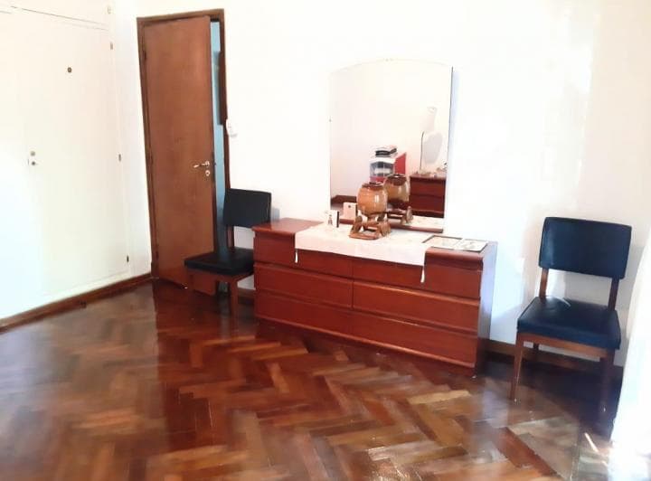 Dormitorio con piso de madera, cómoda con espejo, dos sillas y placard empotrado.