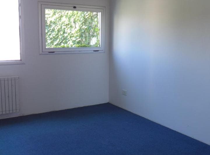 Dormitorio vacío con alfombra azul, radiador y ventana.