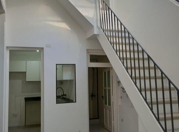 Living con escalera, acceso a cocina y puerta de madera.