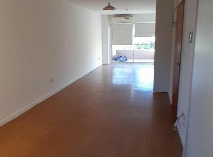Ambiente vacío y luminoso con piso de madera y salida al balcón.
